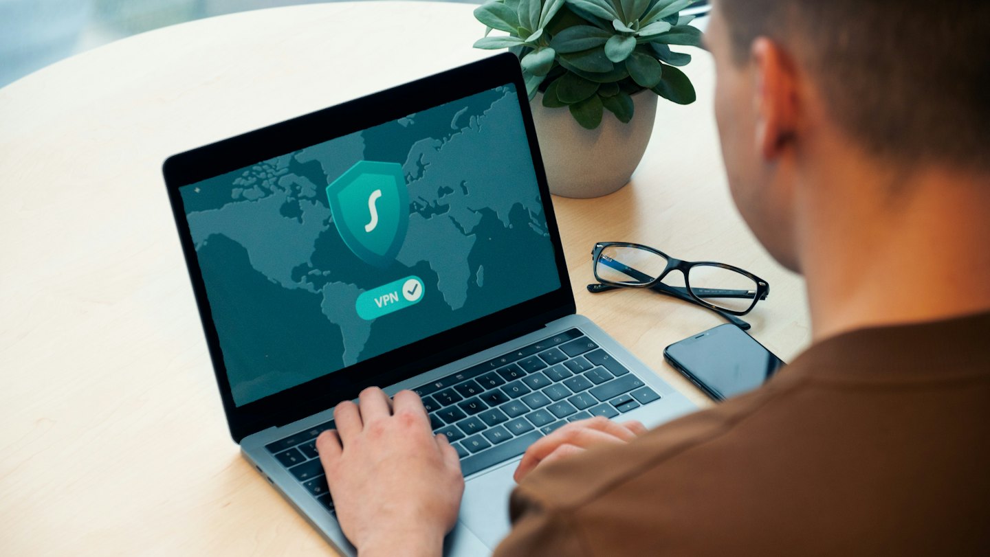 Persoon die een laptop met VPN-verbinding gebruikt op een houten bureau.